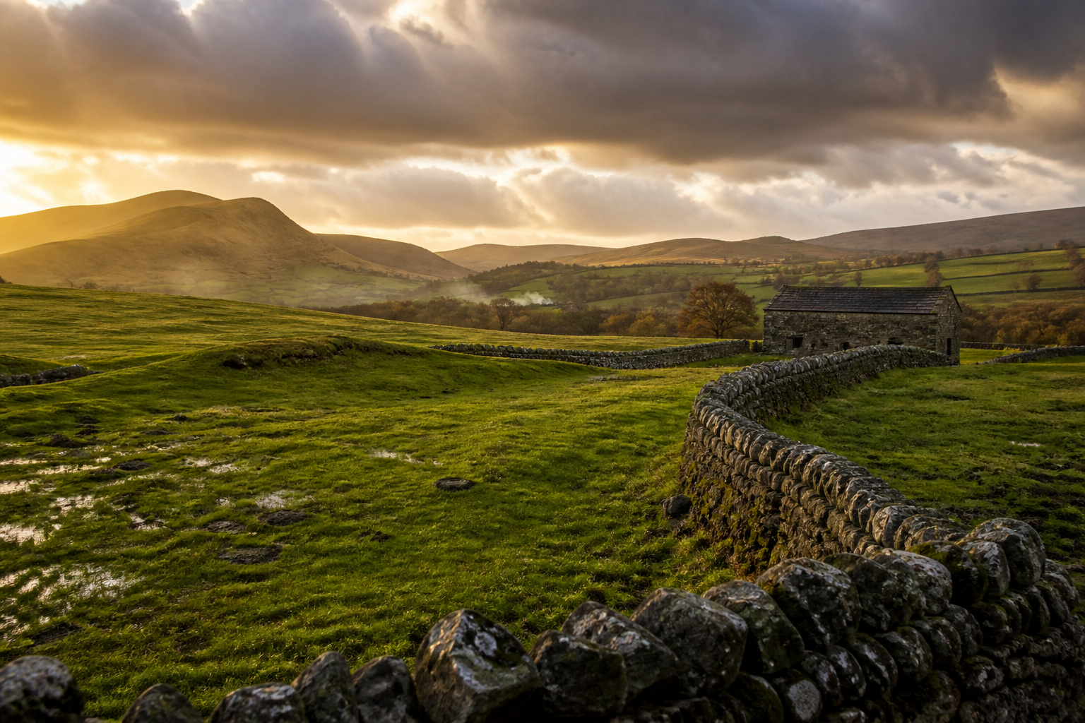 Stone barn beside green hills and a misty valley.